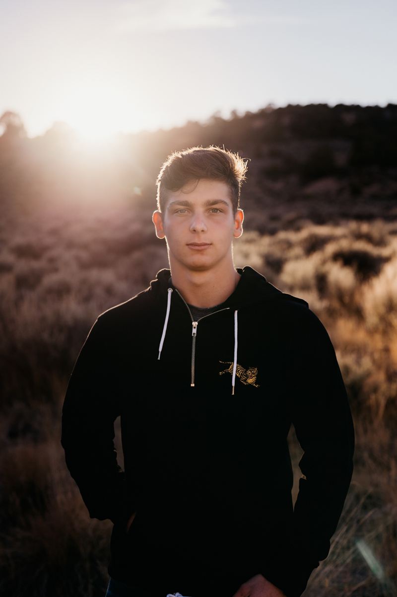 Senior Portrait, High School man wears dark hoodie and stands within a field outdoors