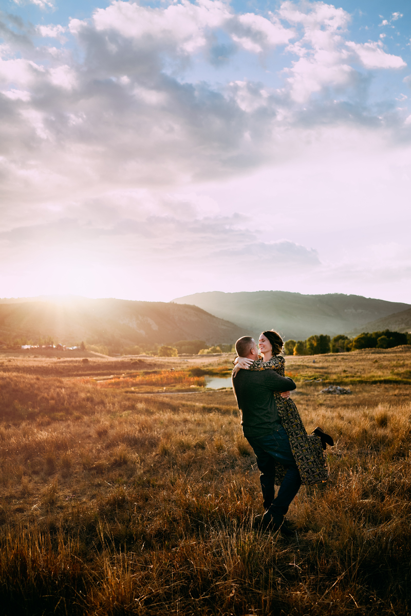 Elopement Photographer, man embraces and swings woman around in a golden grassy field