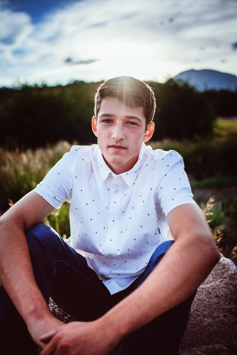 Senior Portrait, High School man with white polo shirt sits outdoors in nature
