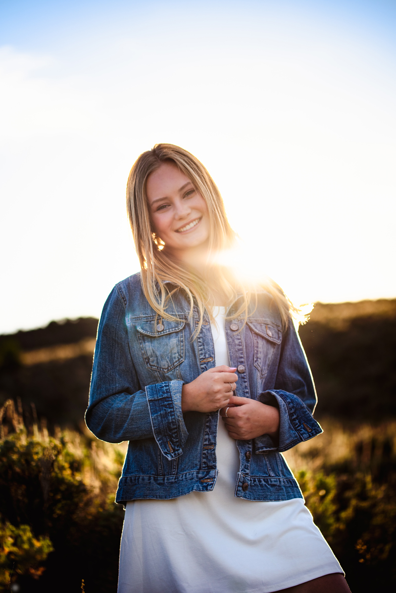 Senior Portrait, High School blonde woman wearing a blue jean jacket and white skirt smiles