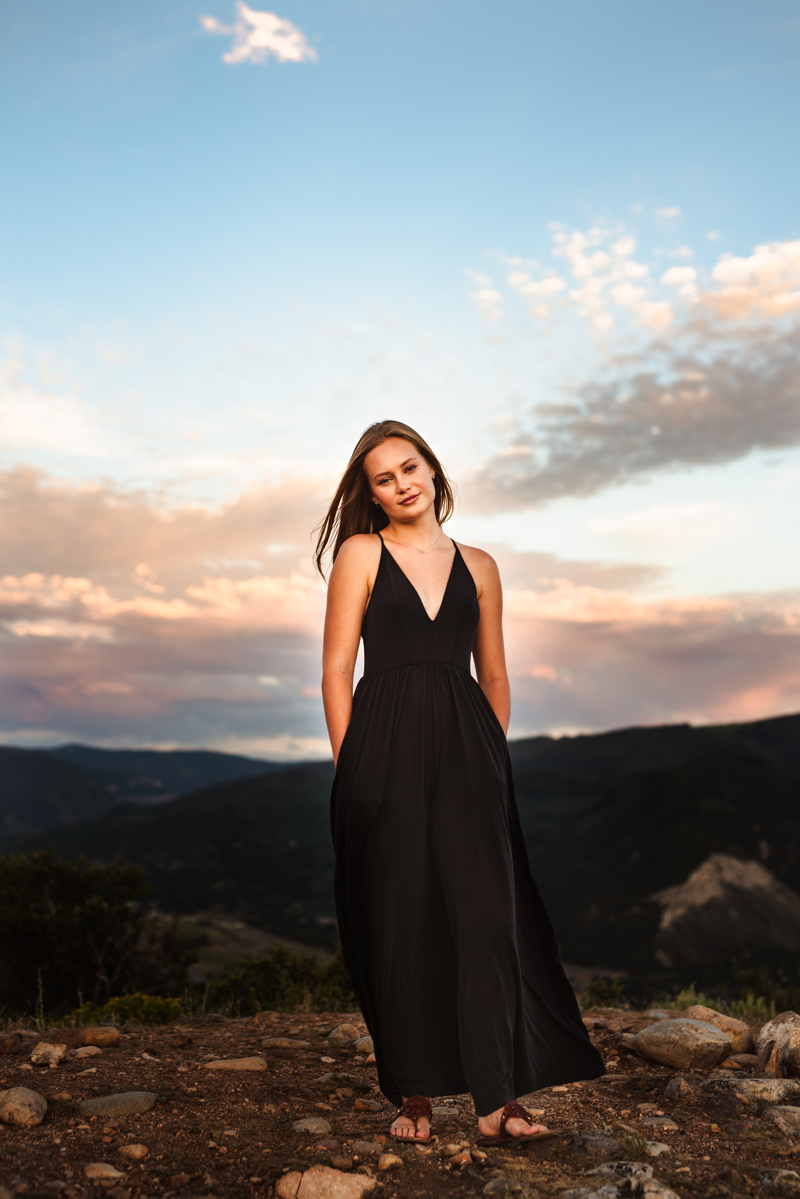 Senior Portrait, High School woman in black dress stands on mountain trail