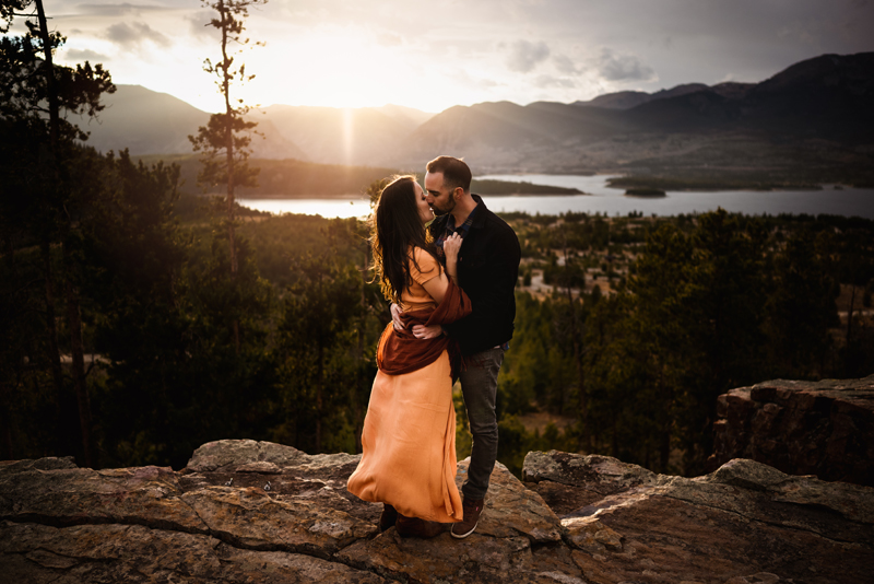Engagement Photographer, man and woman embrace and kiss before a large lake and mountains