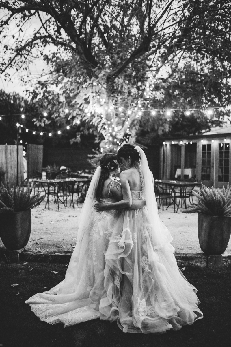 LGBTQ+ Wedding, black and white photo of two brides holding each other close, string lights brighten up an outdoor reception area
