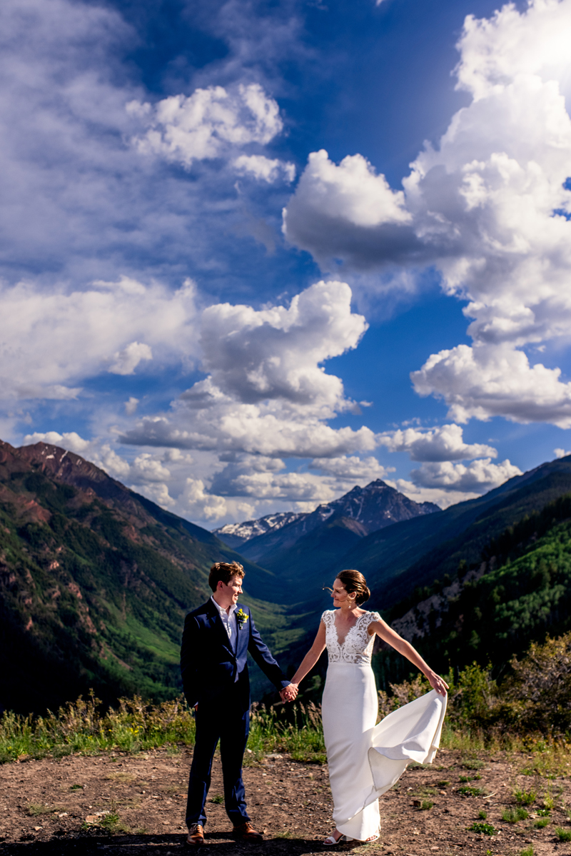 Elopement Photographer, Man and wife in her wedding dress hold hands with mountains behind them