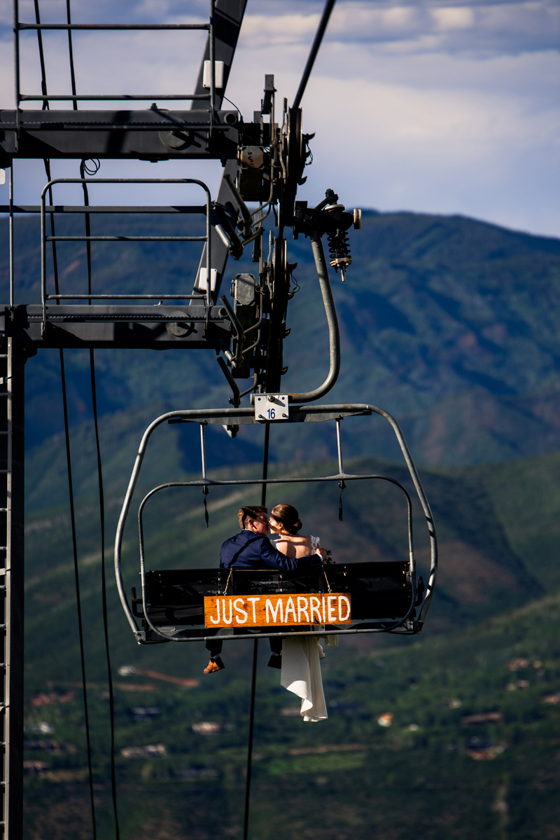 Elopement Photographer, a bride and groom sit on a ski lift kissing, a sign behind them reads just married