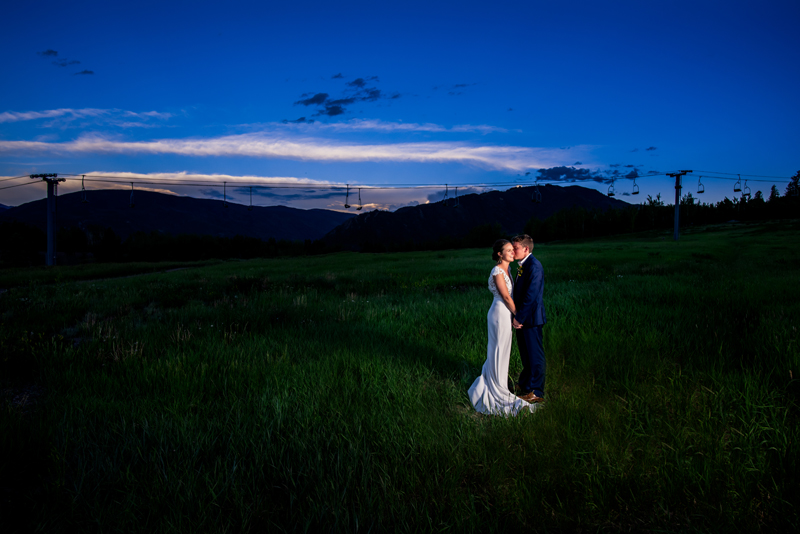 Elopement photographer,  man kisses bride on the cheek on a grassy field at dusk