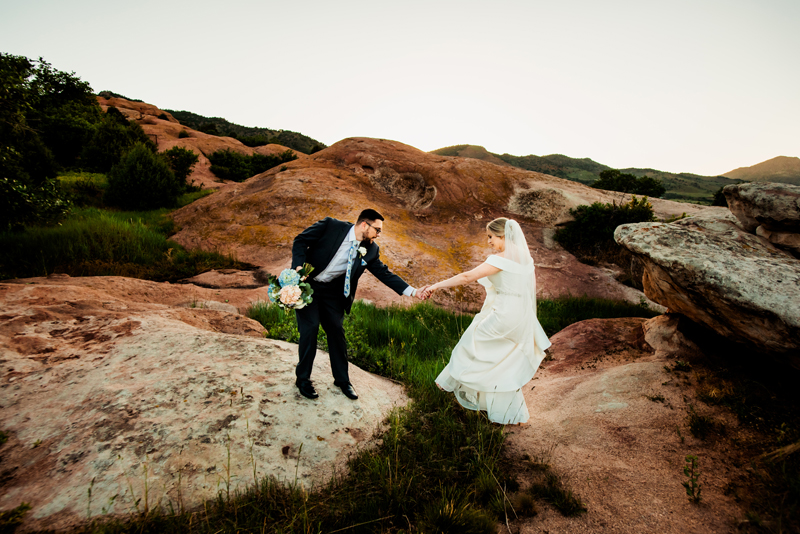 Elopement Photographer, a man holds his brides hand as she skips over a patch of grass in her wedding gown, red rock surrounds them