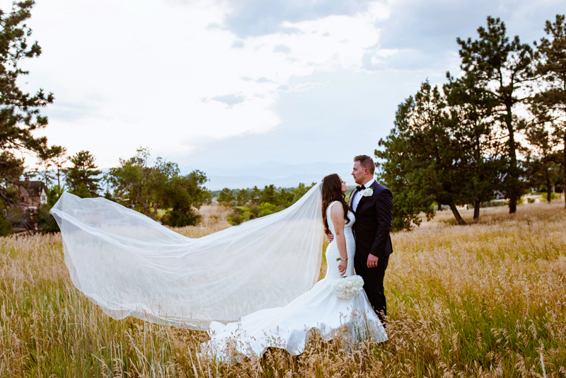 Elopement Photographer, husband holds wife in wedding gown, her long sash blows in the wind, they stand in a grassy meadow